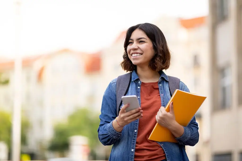 Student holding their phone with books