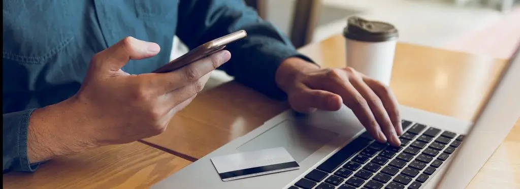 A man using his phone and computer with his credit card on the keyboard